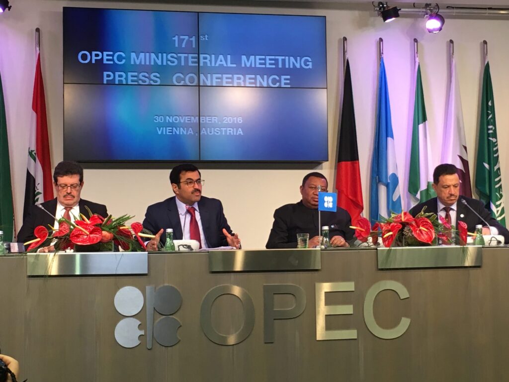 OPEC+ ministers meeting in Vienna discuss oil production cuts at a conference table with energy charts in the background.