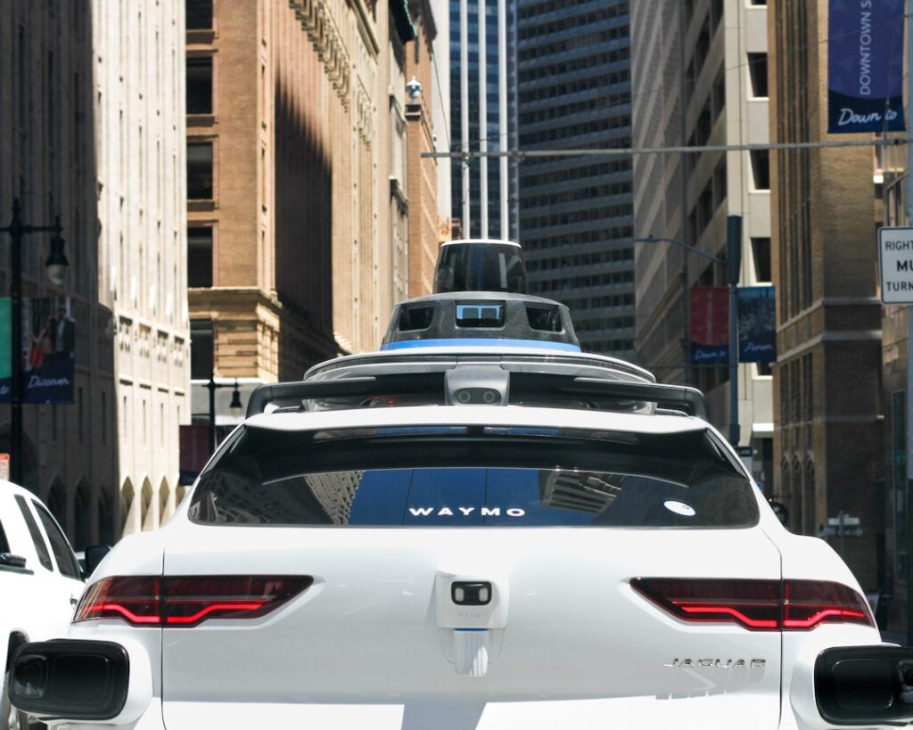 A Waymo autonomous vehicle drives through a city street with no driver behind the wheel during a paid passenger ride.
